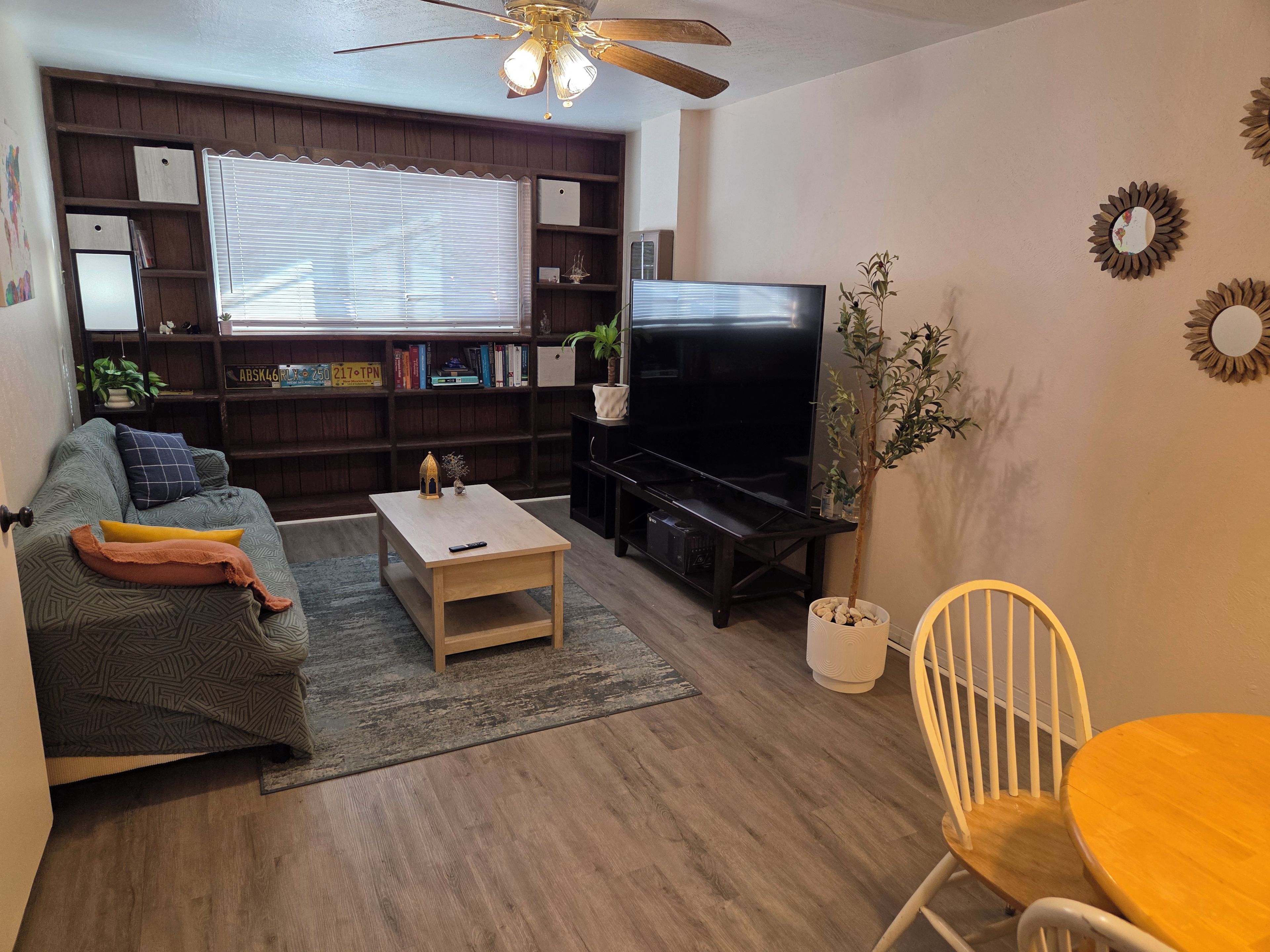 A living room with a sofa, coffee table, TV, bookshelf, and a dining area with a chair and table.
