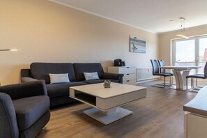 A modern living room with a sofa, coffee table, and a dining area with chairs and a table. - Utholm 2 beach shelter (St. Peter-Ording)