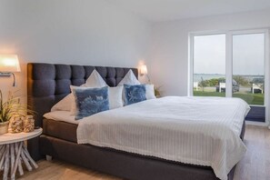 Ein Schlafzimmer mit einem großen Bett, einem runden Beistelltisch und Blick ins Freie durch eine Schiebetür.