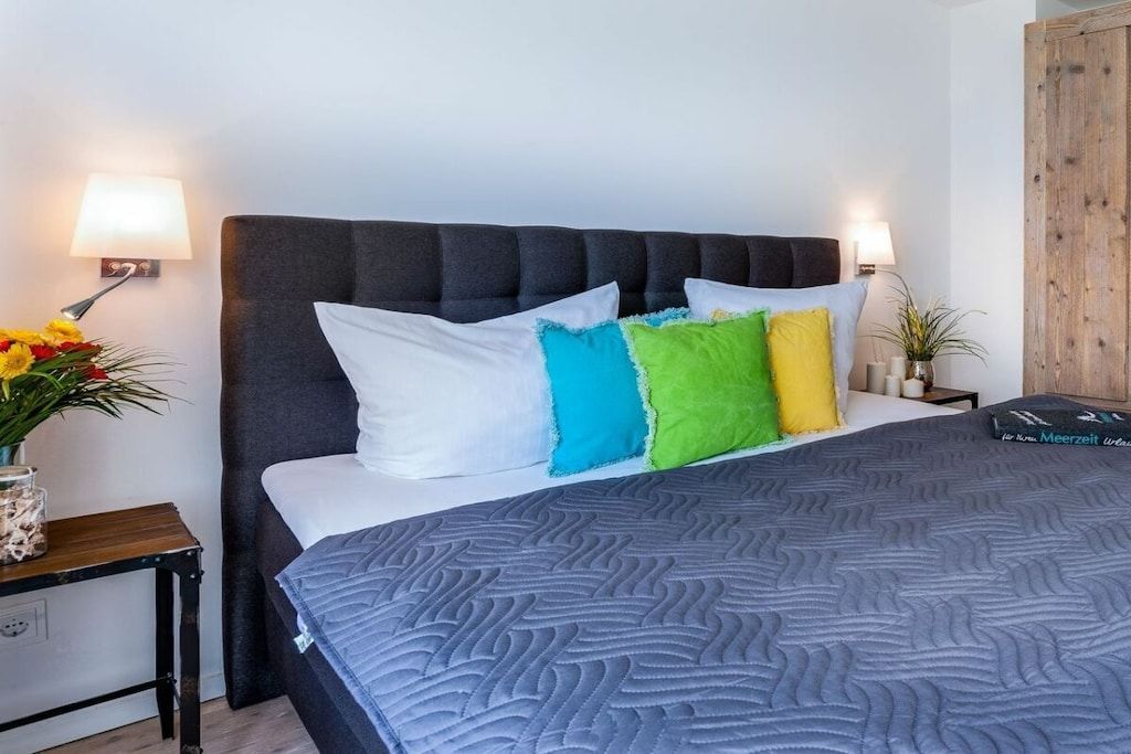 Un lit avec une couette grise, une tête de lit sombre et des coussins colorés.