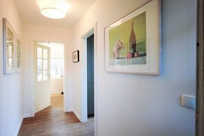 A hallway with a door leading to a room, a framed picture on the wall, and a light fixture above. - Holiday home with 2 bedrooms (Sylt \/ OT Tinnum)
