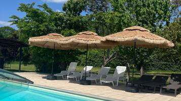 A swimming pool with clear blue water, surrounded by lounge chairs and thatched umbrellas.