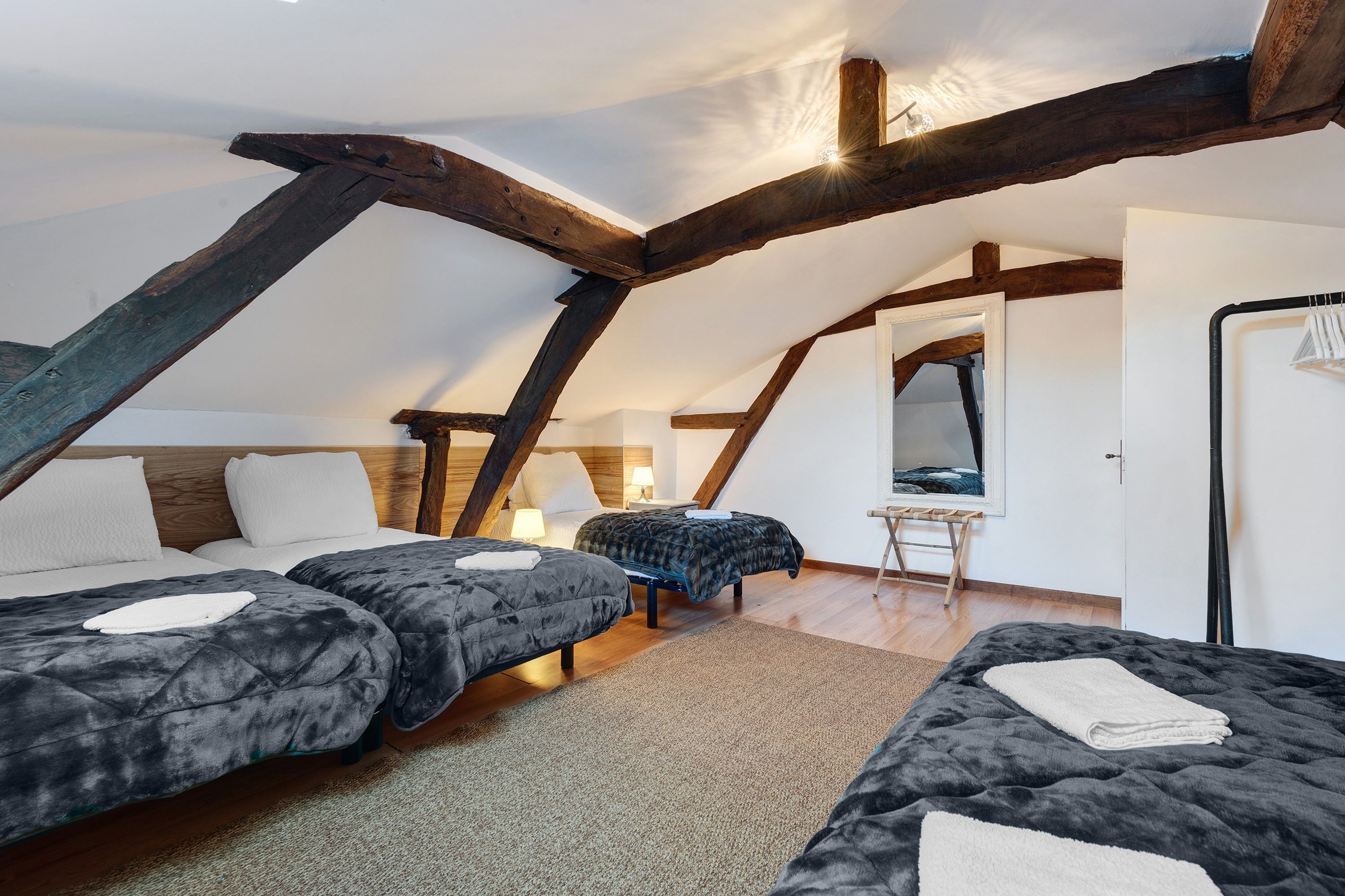 Camera da letto con soffitto spiovente, travi in legno a vista e due letti con biancheria scura.
