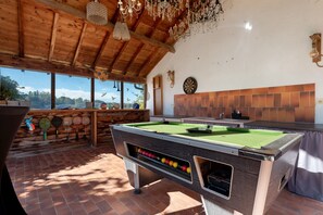 Une table de billard avec des billes, un jeu de fléchettes et une fenêtre donnant sur des arbres.