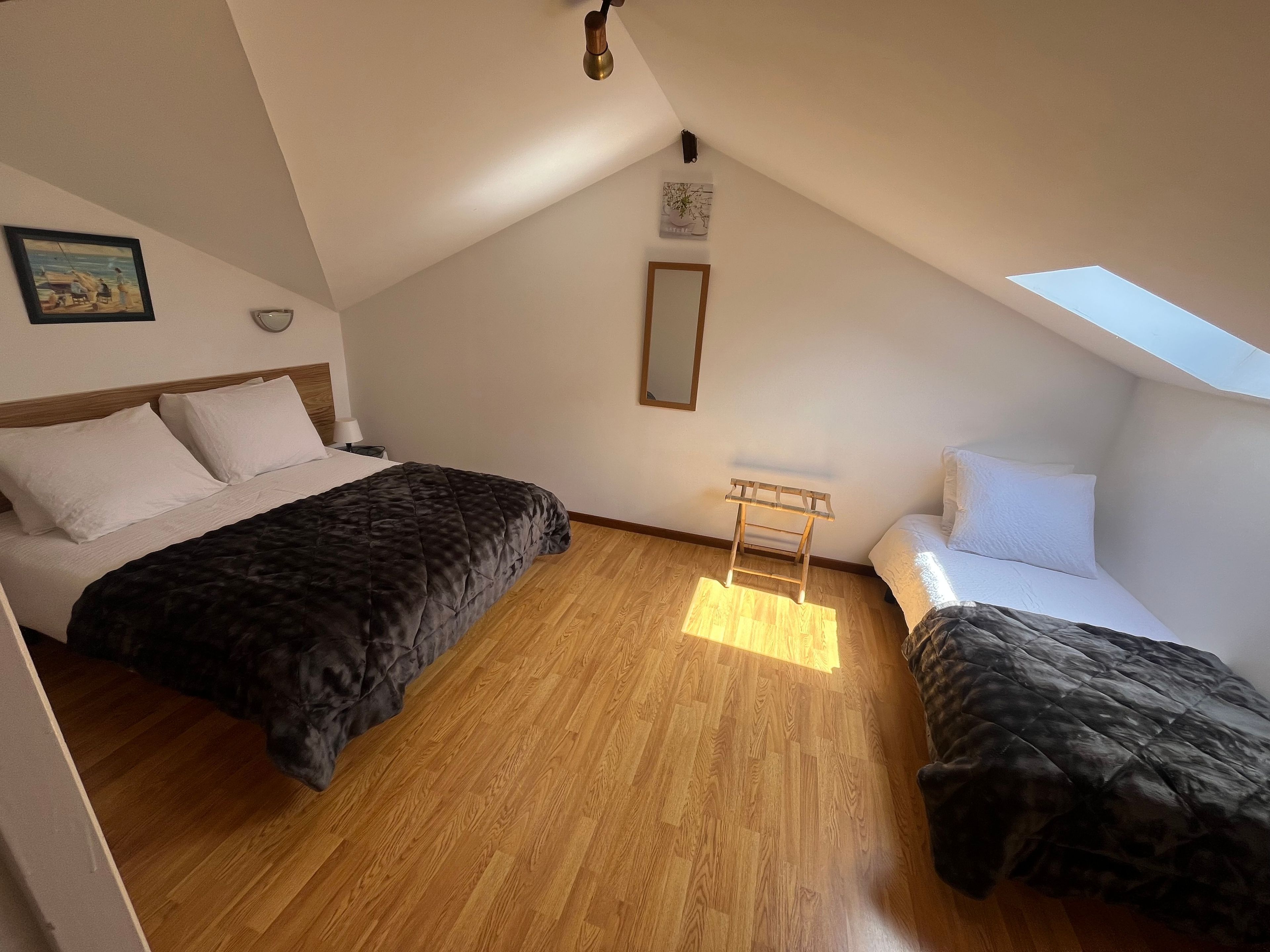 Une chambre avec deux lits, un puits de lumière, un plancher en bois et une petite table.