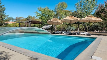 A swimming pool with lounge chairs and umbrellas, surrounded by trees.