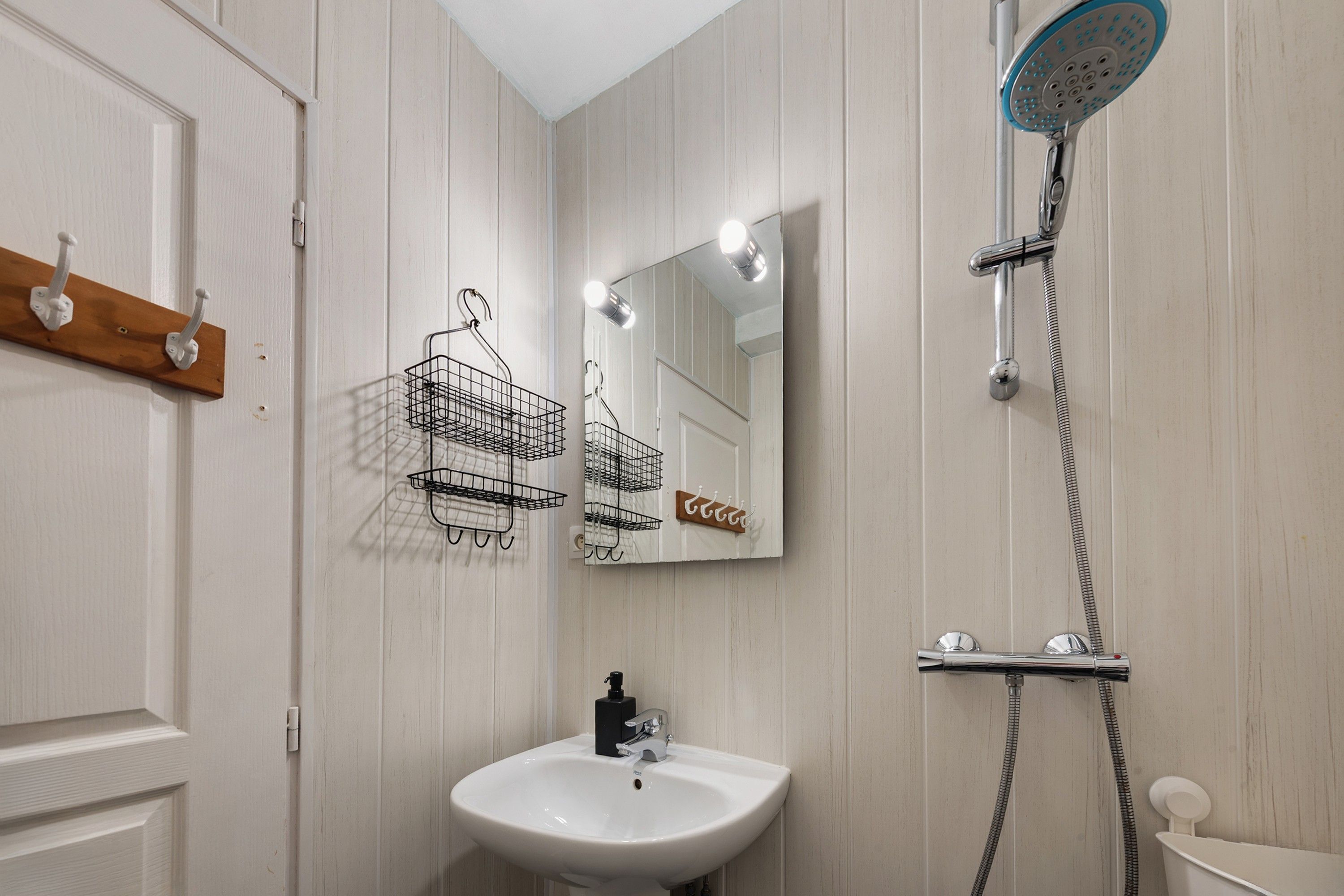A bathroom with a white sink, a mirror, a shower, and a wooden coat rack.