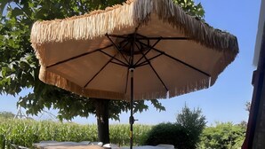 Uma área de refeições ao ar livre com mesa, cadeiras e um guarda-sol de palha.