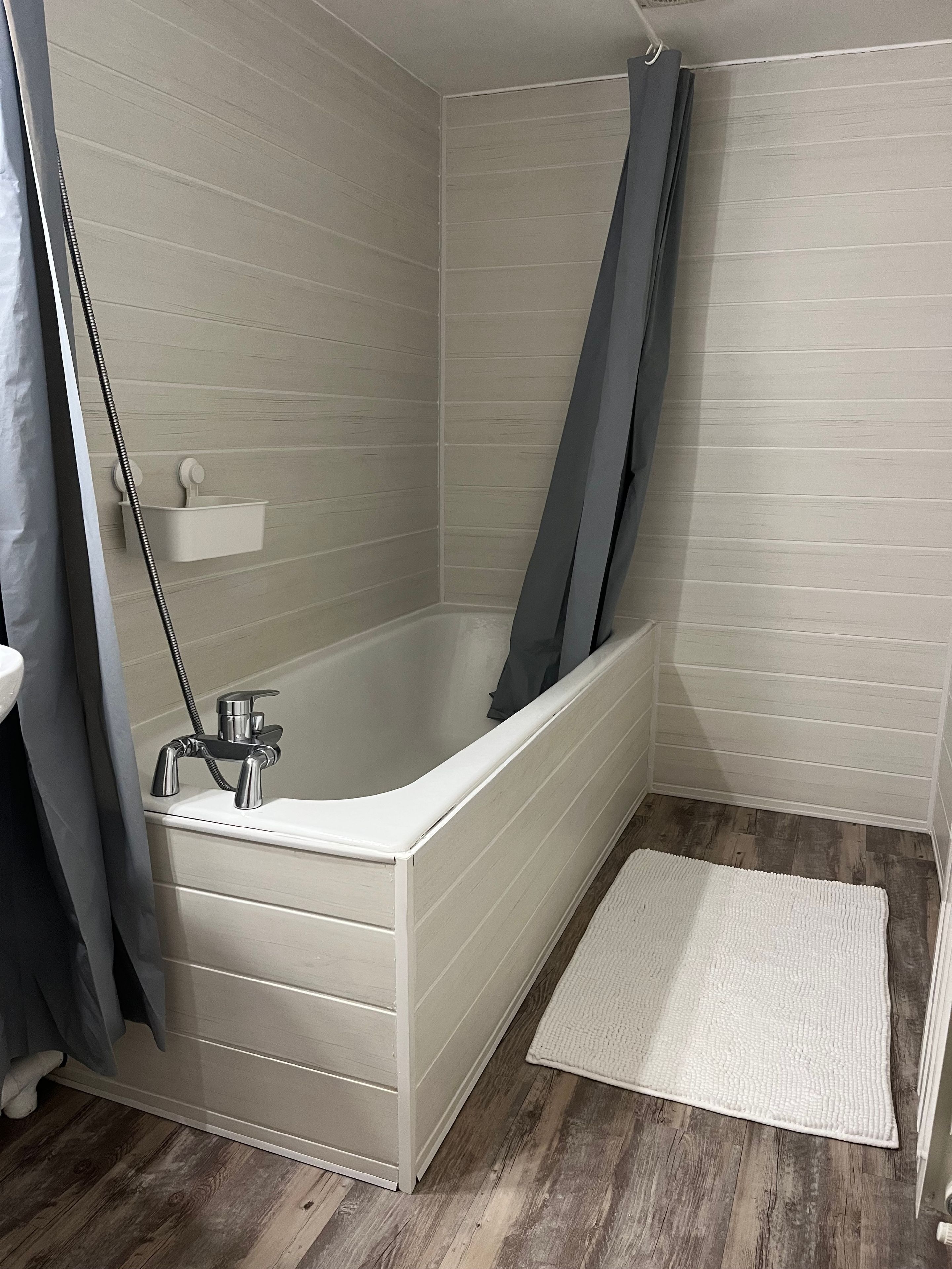 Une salle de bain avec une baignoire, un rideau de douche et un tapis blanc.