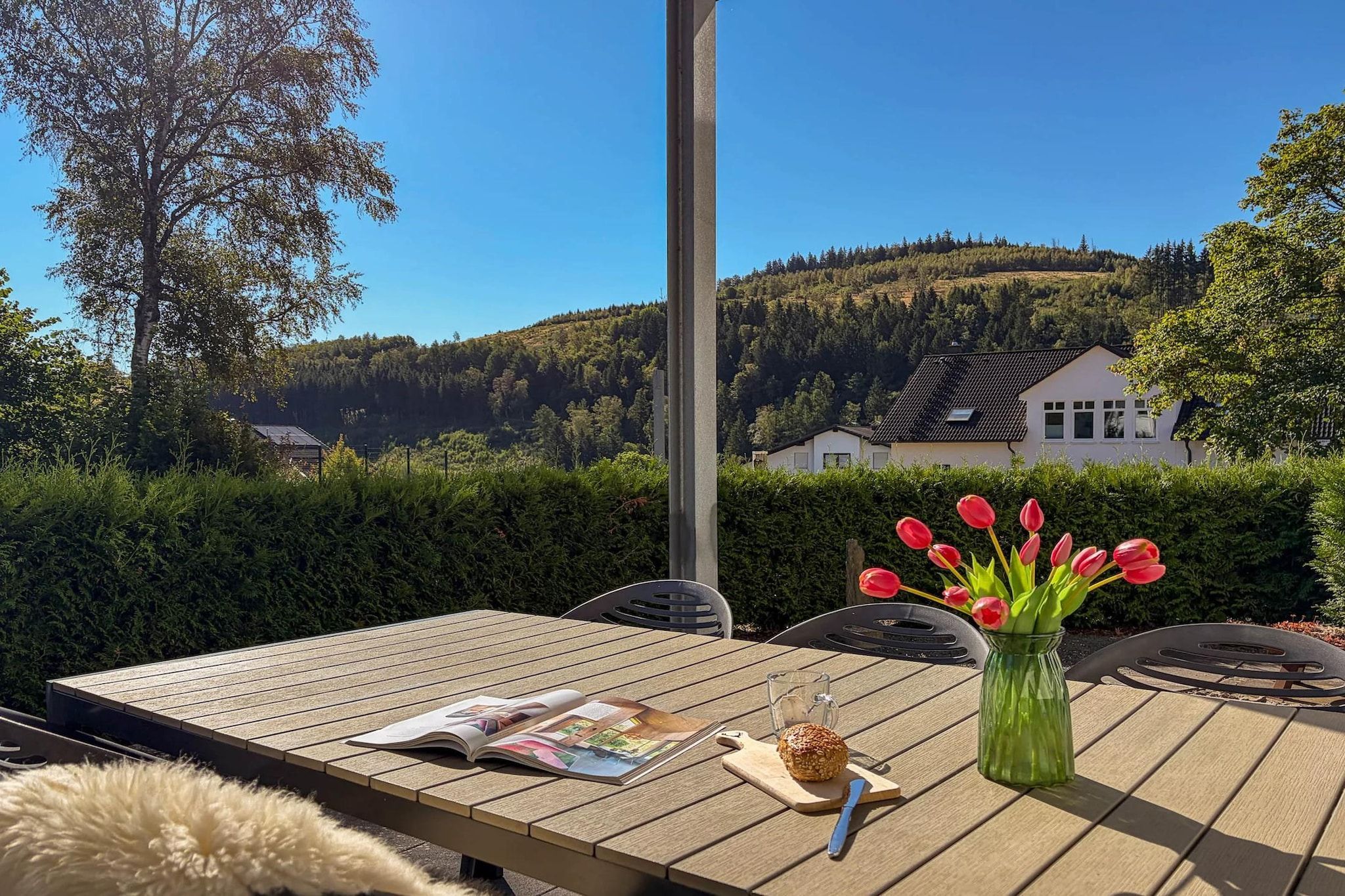 An outdoor table with a magazine, a glass jar, and a tulip arrangement.