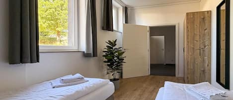 Habitación de hotel con dos camas, una planta en maceta y vistas al exterior.