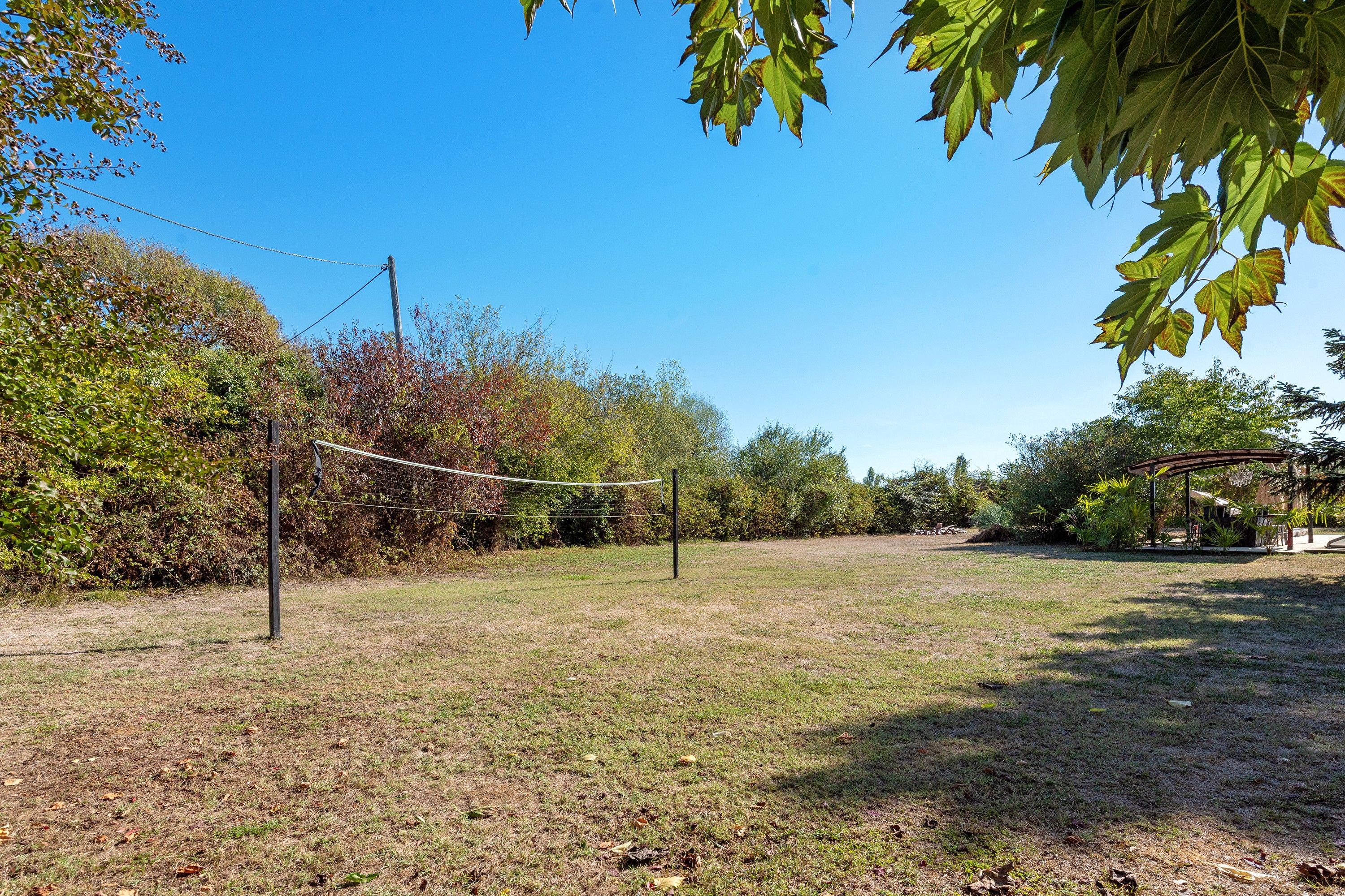 A volleyball net in a grassy area with trees and a wooden structure in the background.