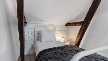 Een kleine, knusse slaapkamer met een eenpersoonsbed, een nachtkastje met lamp en een ventilator aan de muur.