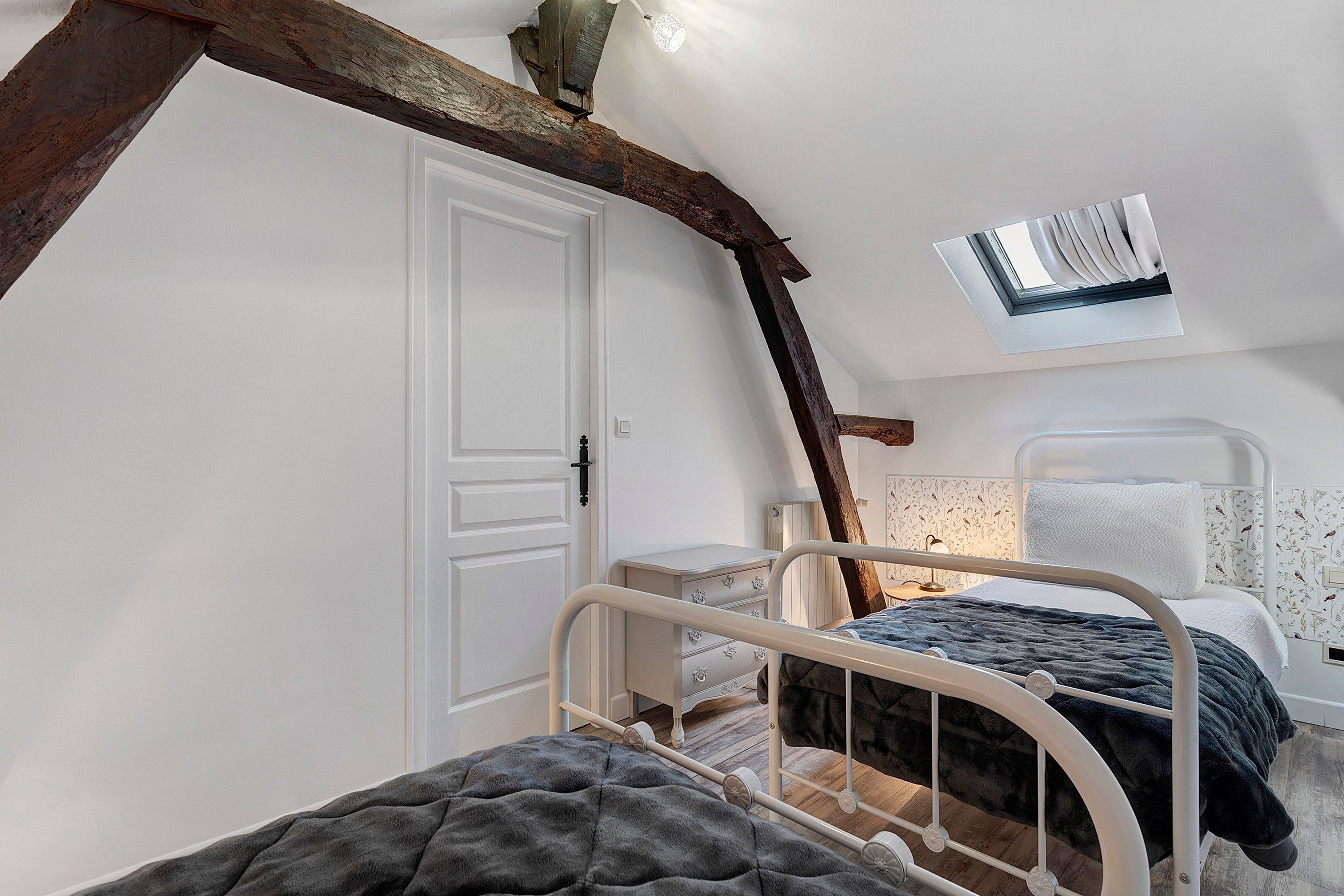 Un dormitorio con techo inclinado, una cama con cabecera, un aparador y una puerta.