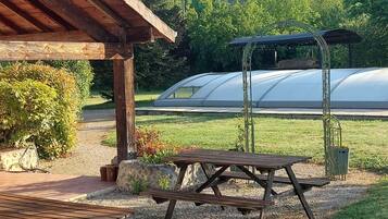 Un espace extérieur abrité, doté de tables de pique-nique, avec une serre en arrière-plan.