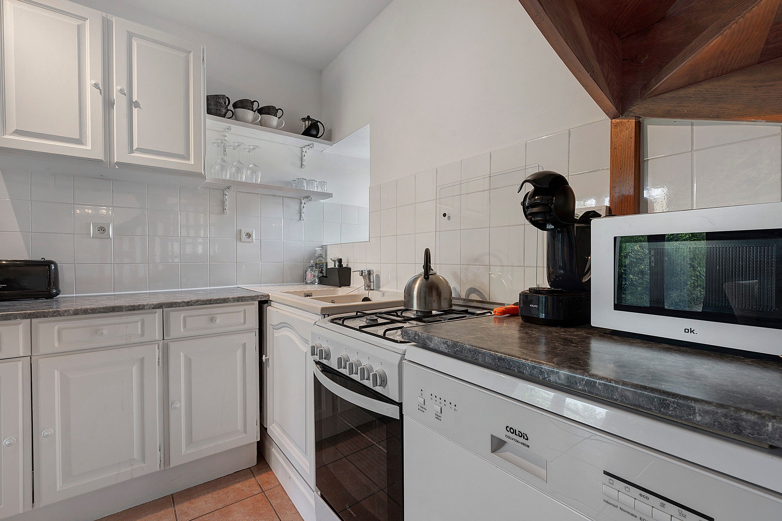 A modern kitchen with white cabinetry, a gas stove, a coffee maker, and a built-in oven.