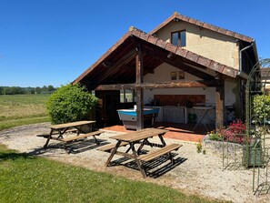 Una casa rústica con techo inclinado, cocina al aire libre cubierta y mesas de picnic.