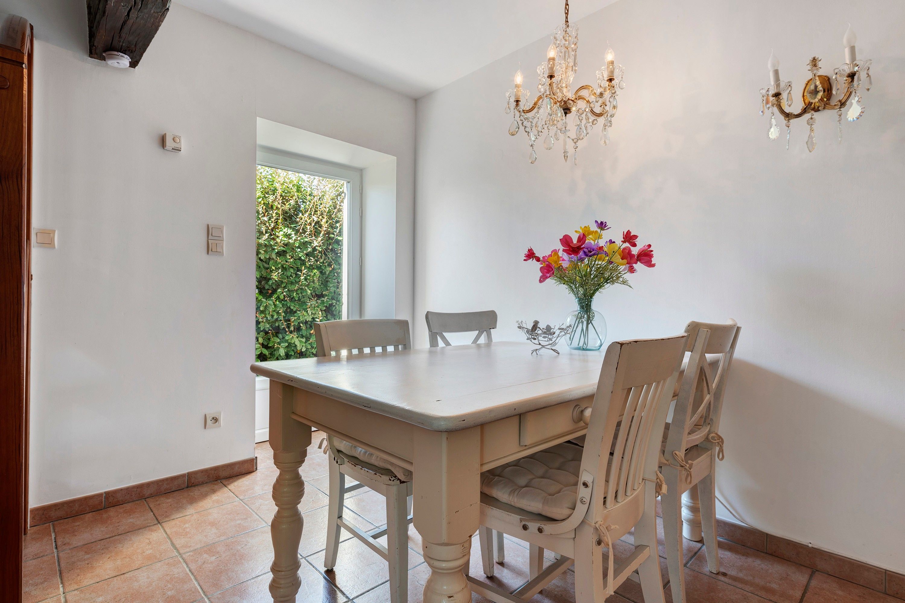 Ein Essbereich mit Tisch, Stühlen, einer Chandelüster und einer Blumenvase.