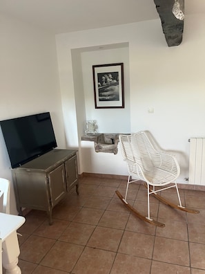 Una habitación con televisor en un mueble, una mecedora, un cuadro en la pared y un elemento decorativo de pared de piedra.