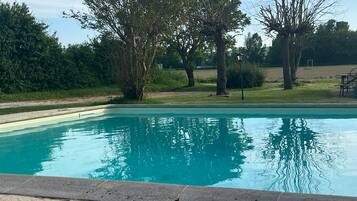Une piscine à l’eau claire, entourée d’arbres et bordée d’une pelouse.