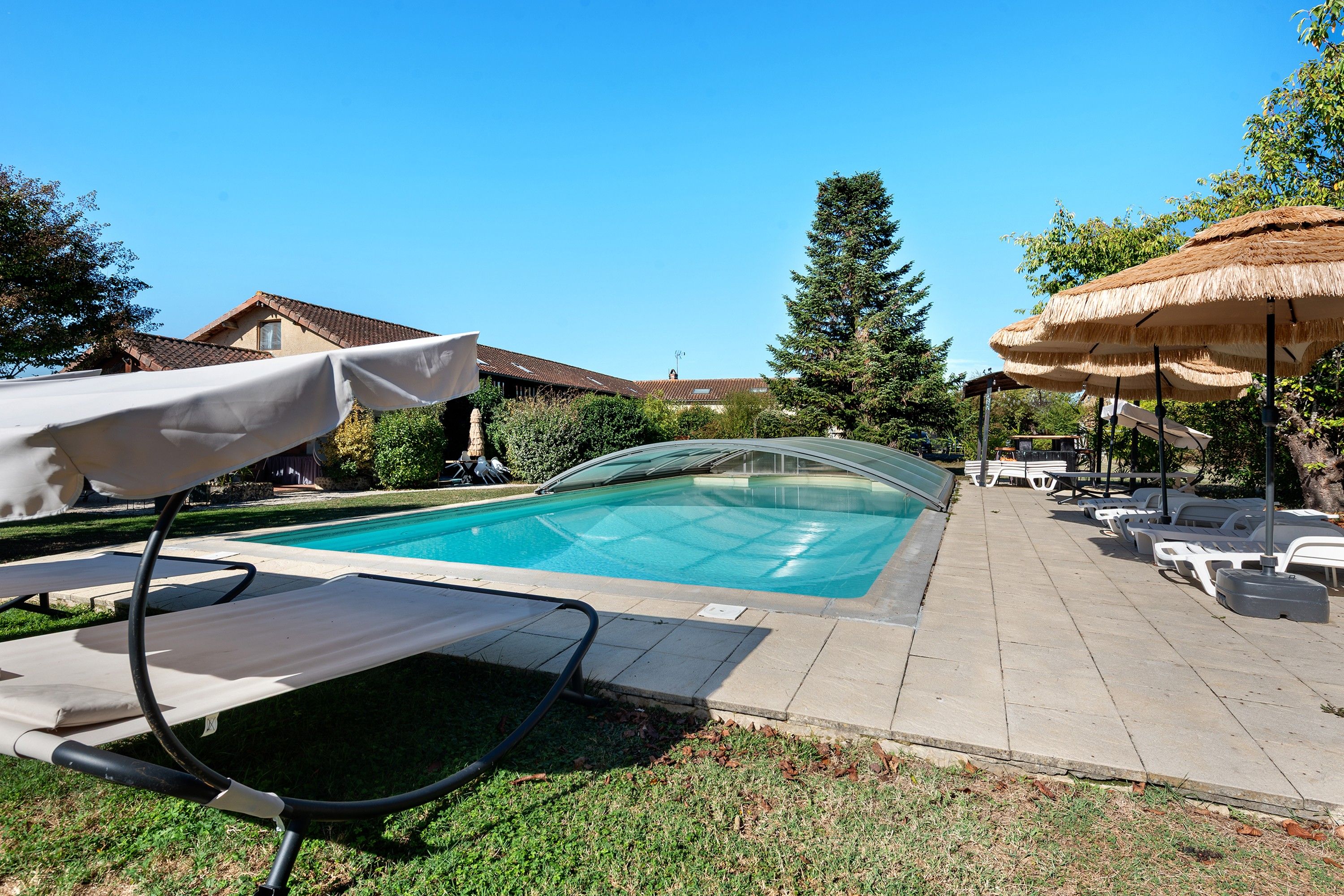 A swimming pool with lounge chairs and umbrellas, surrounded by grass and trees.
