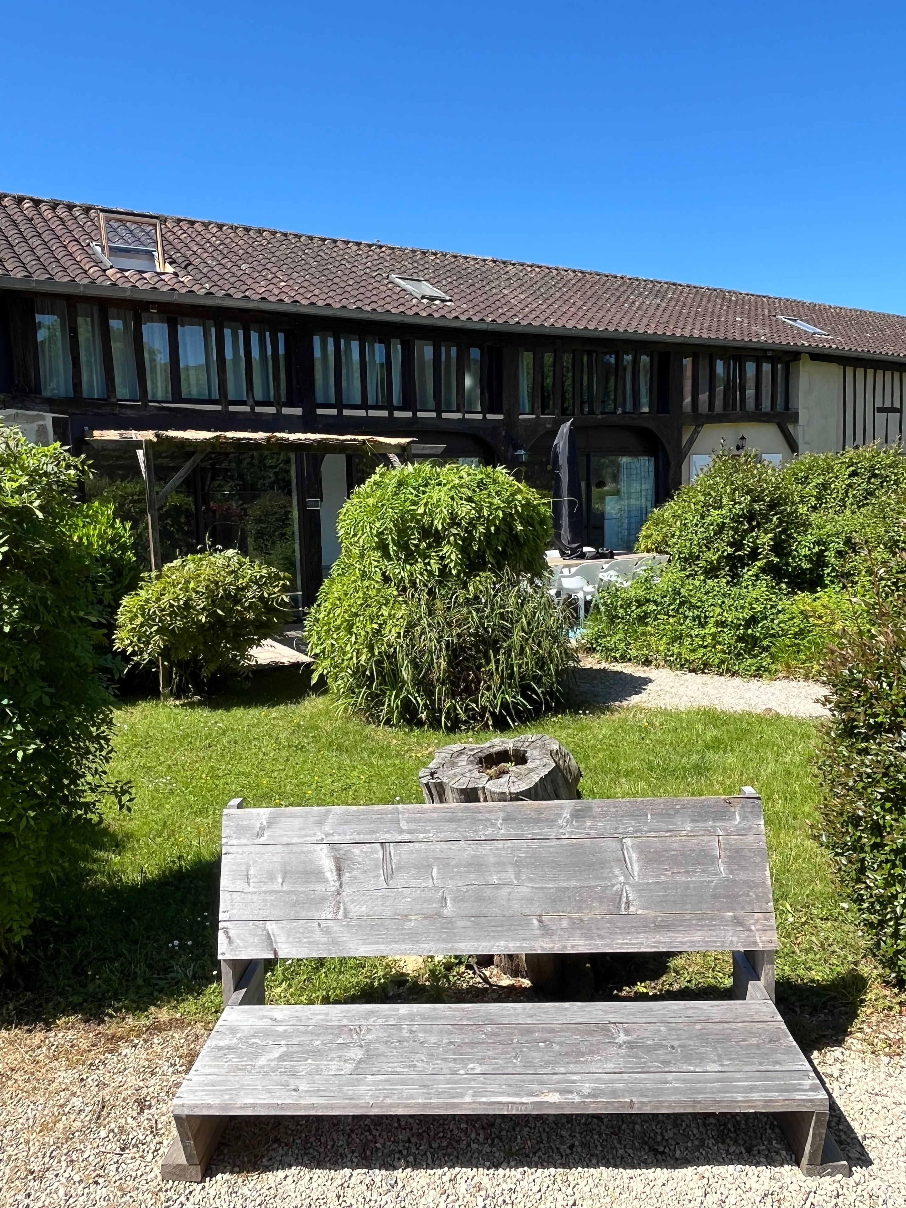Un banc en bois dans un jardin, avec un bâtiment visible à l’arrière-plan.