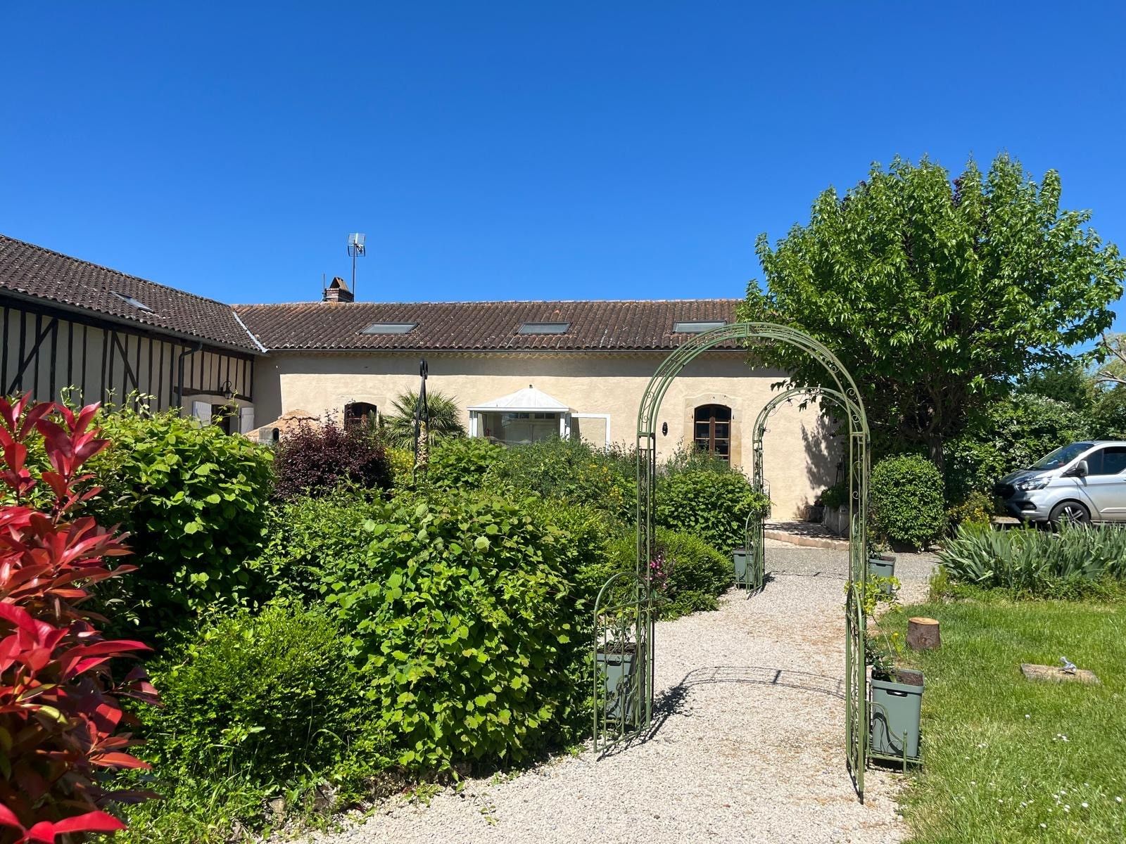 Un sentier de jardin qui mène à un bâtiment doté d’un toit en tuiles et d’une entrée abritée.