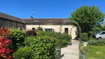 Un sentier de jardin qui mène à un bâtiment doté d’un toit en tuiles et d’une entrée abritée.