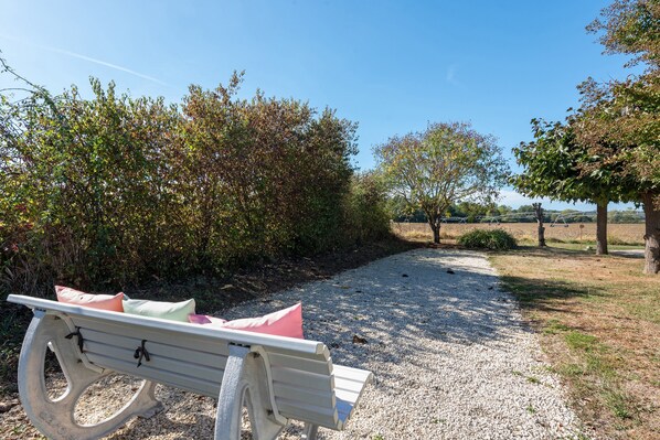 A gravel path with a bench and a picnic table, surrounded by trees and shrubs.