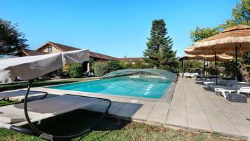 A swimming pool with lounge chairs and umbrellas, surrounded by grass and trees.