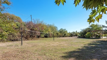 A volleyball net in a grassy area with trees and a wooden structure in the background.