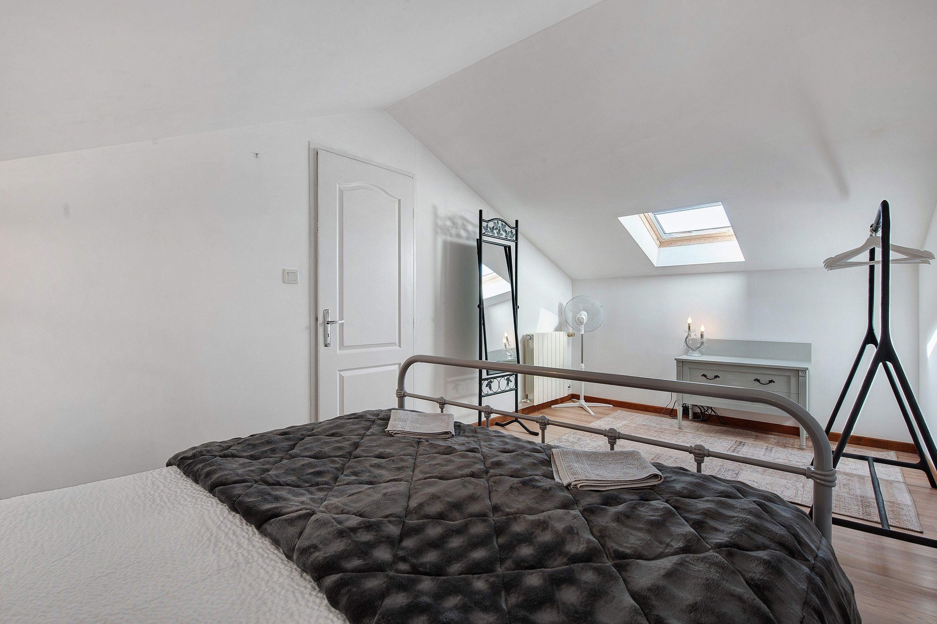 Un dormitorio con cama, cómoda, radiador y tragaluz.