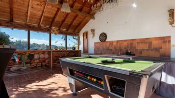Una mesa de billar con bolas, un dardo y una ventana que da a un paisaje de árboles.