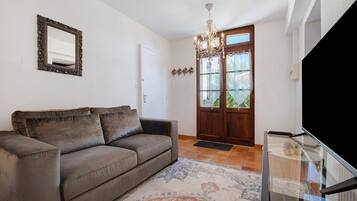 A living room with a sofa, a chandelier, a door with glass panels, and a television on a stand.