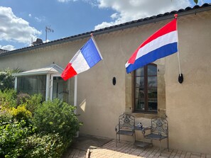A building with a beige exterior, a glass door entrance, and two metal chairs outside. - Holiday Home “Domaine Logis Gascogne, Gîte 2”: Garden View, Pool, Wi-Fi (Saint-Justin)