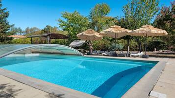 A swimming pool with lounge chairs and umbrellas, surrounded by trees.