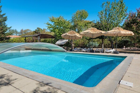 A swimming pool with lounge chairs and umbrellas, surrounded by trees.