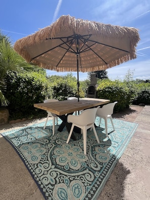 A patio with a wooden table, white chairs, and a thatched umbrella. - Holiday Home “Domaine Logis Gascogne, Gîte 2”: Garden View, Pool, Wi-Fi (Saint-Justin)