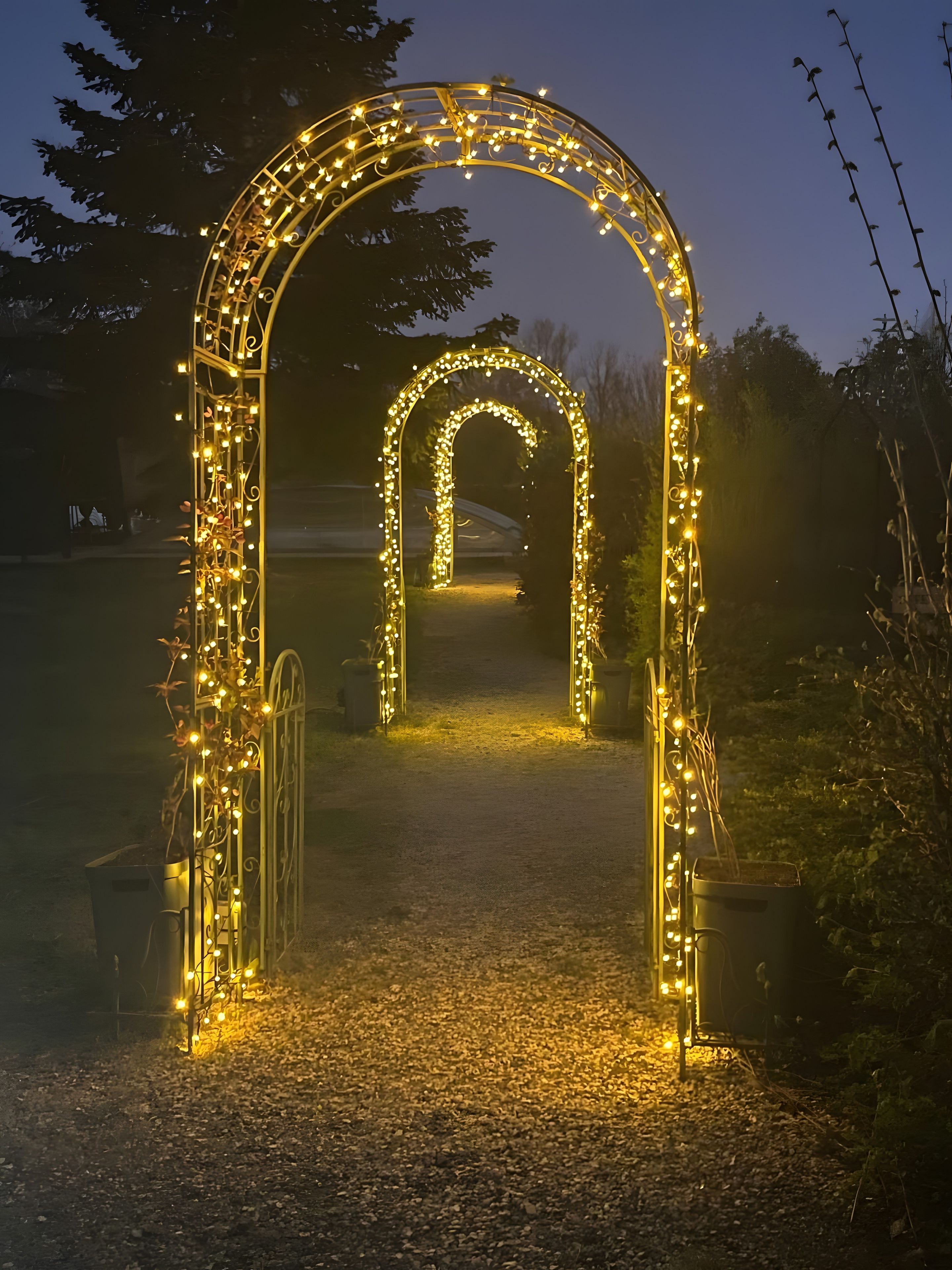 Ein Pfad mit einem beleuchteten Torbogen, umgeben von Vegetation und einem Kiesweg.