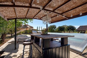 An outdoor patio with a bar area, seating, and a pool.