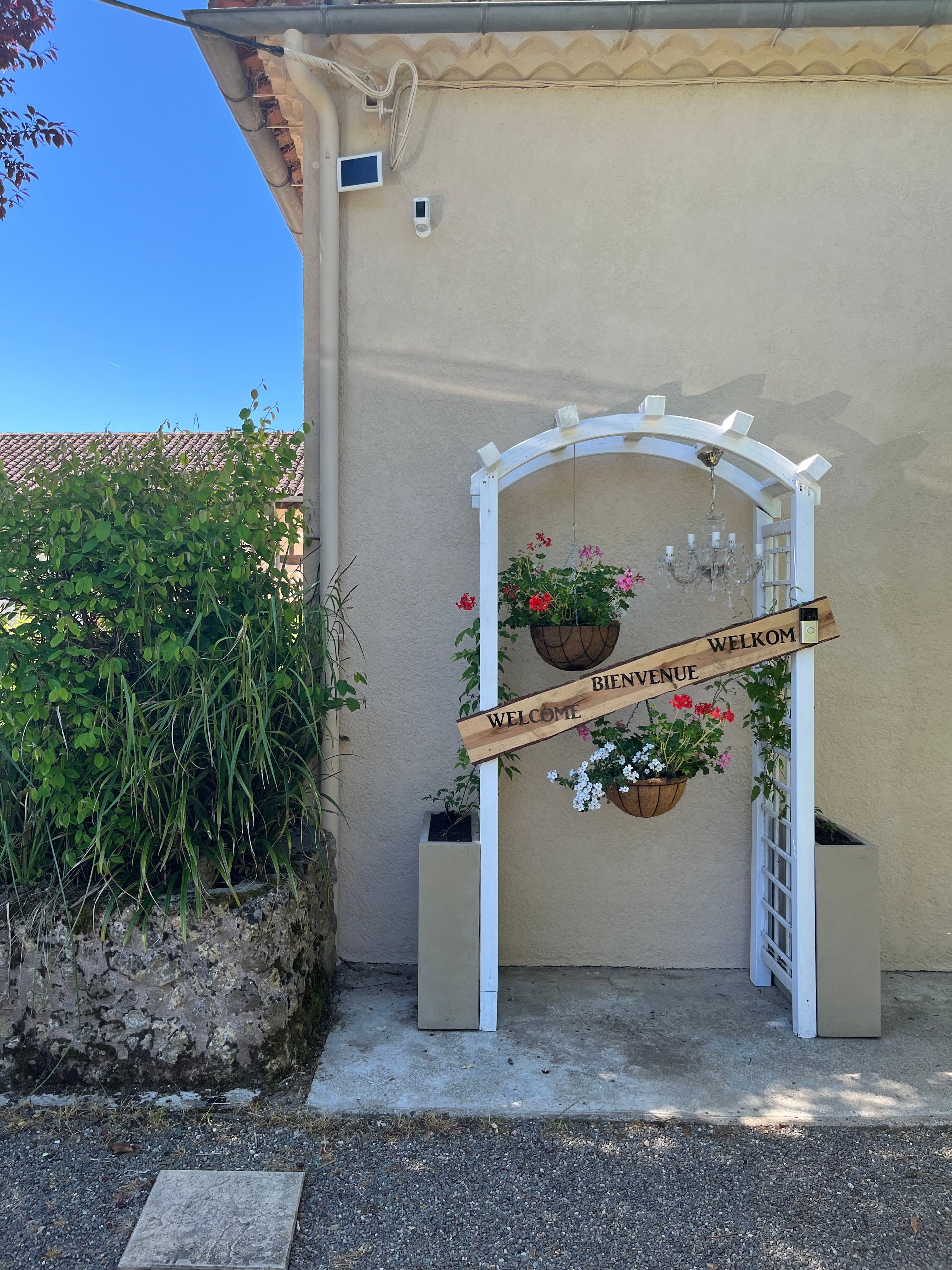 A welcome sign with a wooden archway, potted plants, and a clear blue sky.