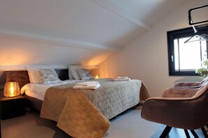 Un dormitorio con cama, lámparas de noche, una silla y una ventana.