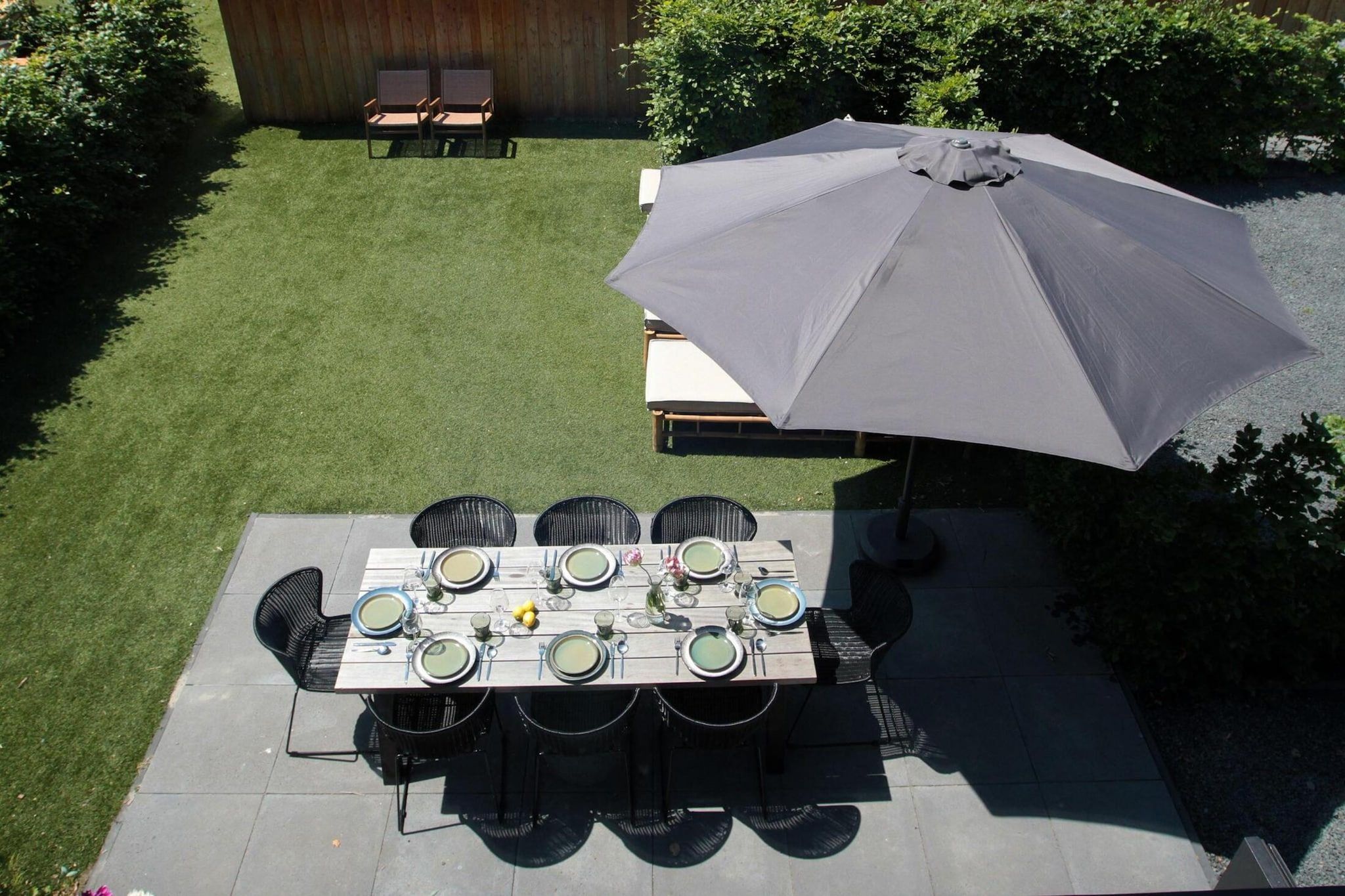 A patio with a table set for four, surrounded by chairs, and an umbrella providing shade.