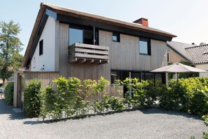 Ein modernes, zweistöckiges Haus mit Schrägdach, einer Holzterrasse und einer Schotterauffahrt.