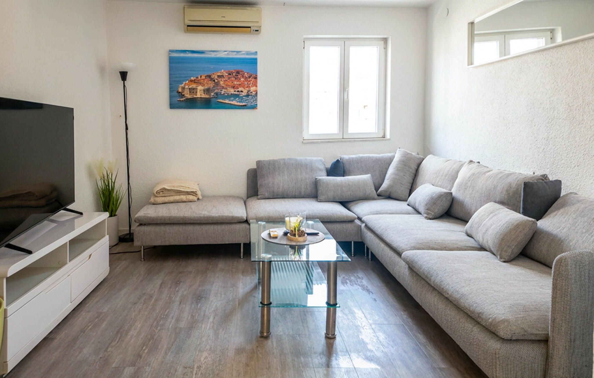 Ein Wohnzimmer mit einer Couch, einem Glastisch, einem Fernseher und einem Gemälde mit einer Küstenlandschaft.