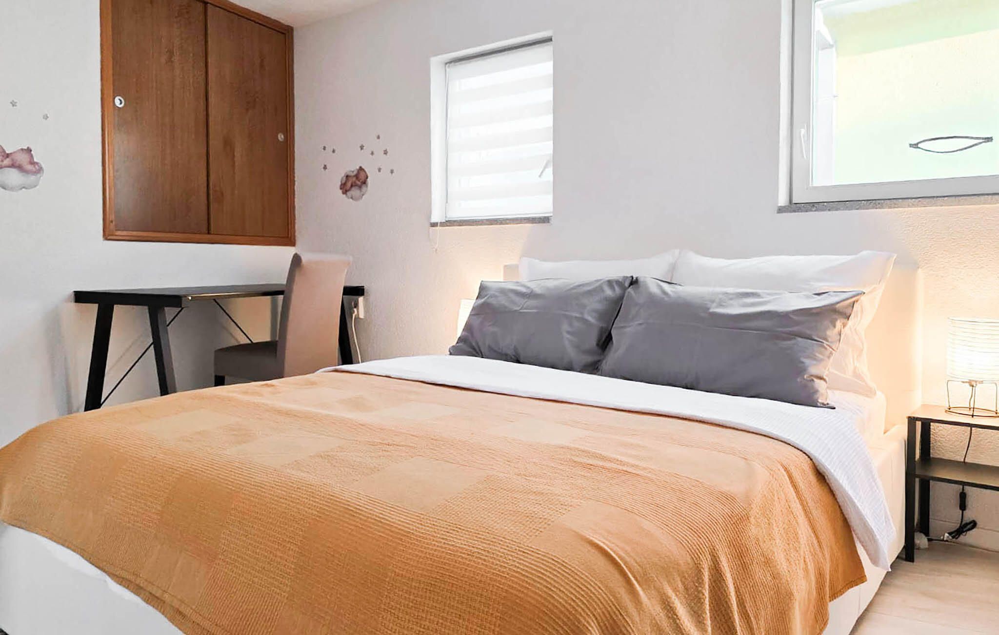 A bedroom with a bed, a desk, and a window.