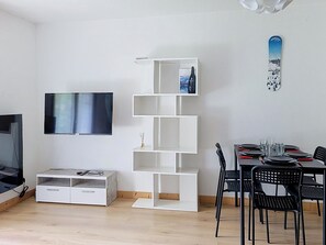 Ein modernes Wohnzimmer mit einem Flachbildfernseher, einer weißen Regaleinheit, einem Esstisch mit Stühlen und einer Snowboard-Dekoration an der Wand.