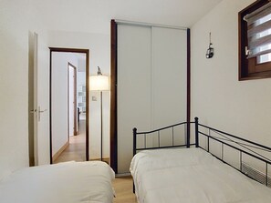 Une chambre avec deux lits, une armoire, une lampe et une fenêtre avec des stores.