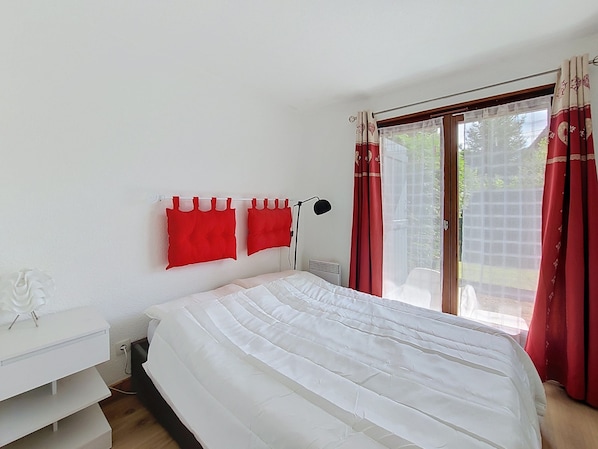 Ein Schlafzimmer mit einem Bett, einem Nachttisch, einer Lampe und einem Fenster mit Vorhängen.