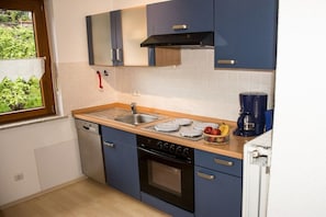 A compact kitchen with a dishwasher, stove, and a coffee maker. - Holiday apartment in Rhön with 1 bedroom (Hilders)